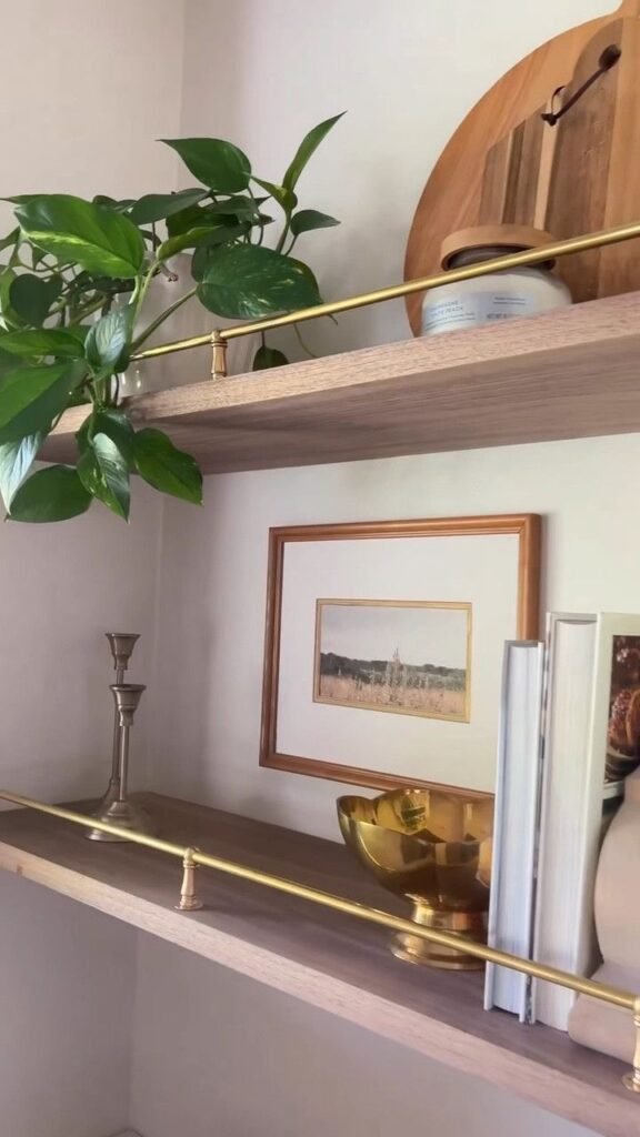 Modern brass picture ledge holding layered art frames and candles above a headboard.