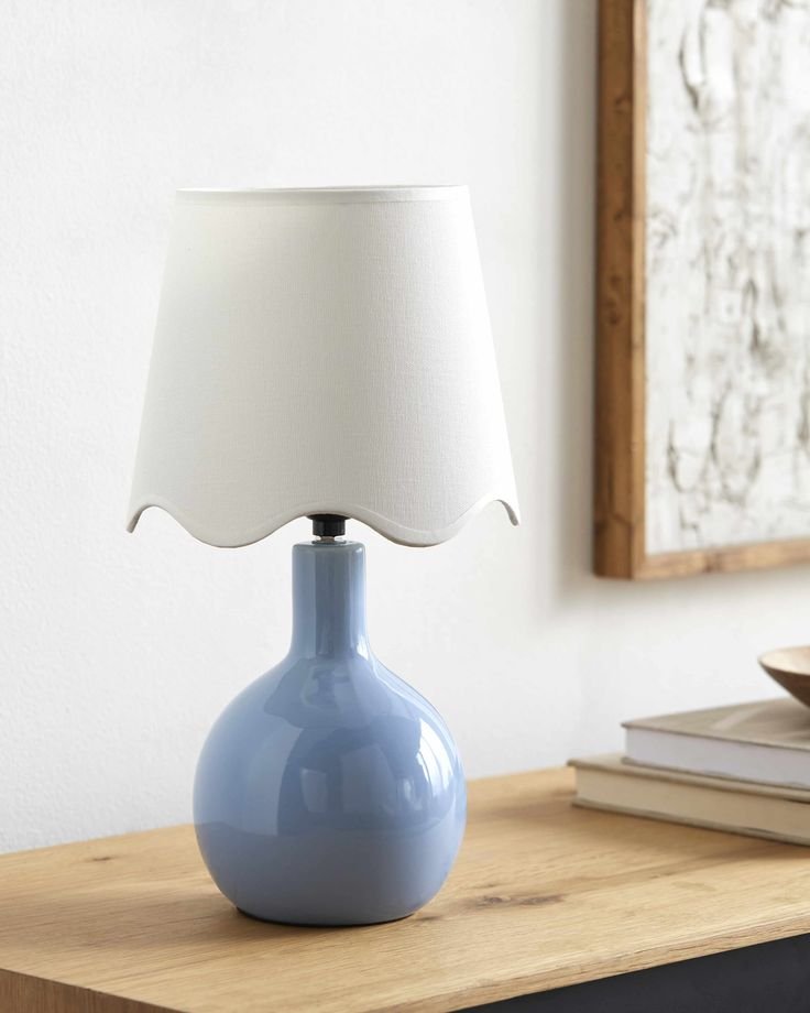 Ceramic table lamp with a smooth, rounded base and decorative scalloped top edge, topped with a light fabric shade and casting a warm, inviting glow.