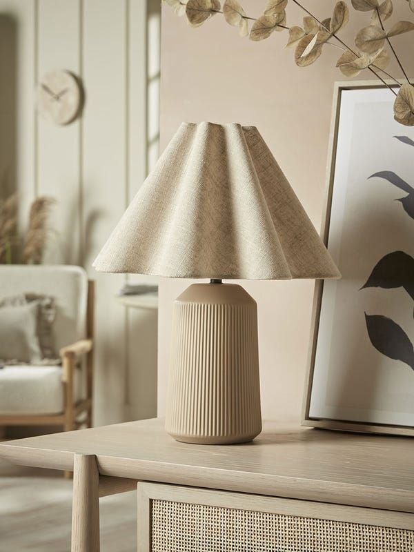 Soft, creamy linen table lamp with a wavy, cloud-like shade that diffuses warm light, set on a minimalist wooden base on a bedside table, creating a cozy, airy atmosphere.