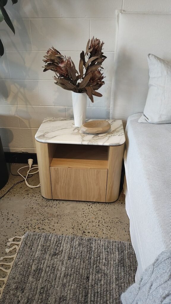 A luxury bedside table featuring a polished white marble top with grey veining and a sturdy base.