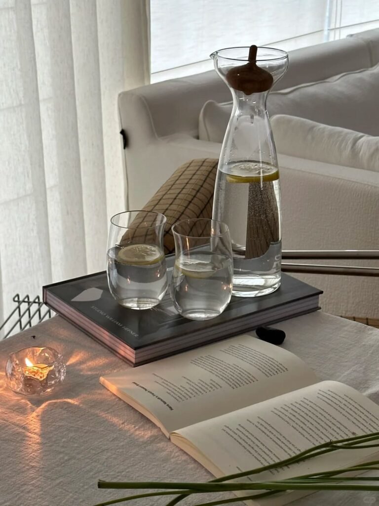 living room table styled with an elegant glass water carafe and matching drinking glass.